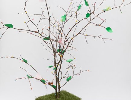 Fotografia drzewka emausowego.  Na gałęziach zielone listki, ptaszki, drobne kolorowe ozdoby.