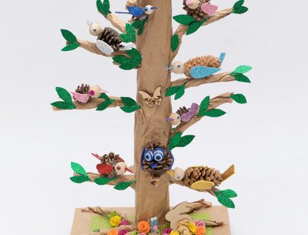 Fotografia drzewka emausowego. Różnokolorowe ptaszki na każdej gałęzi. Na szczycie gniazdo z jajkami.