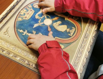 Kolorowe zdjęcie. Tyflografika oglądana przez osobę w różowej kurtce, widać tylko ręce. Tyflografika przedstawia projekt herbu wykonany przez Jana Matejkę, na co dzień znajduje się na wystawie stałej w Pałacu Krzysztofory.