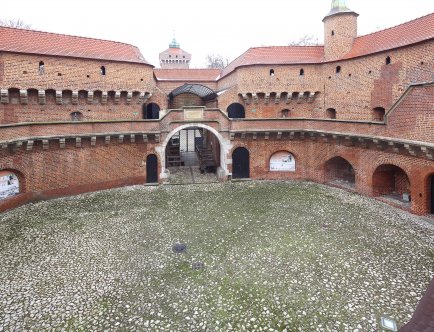 Kolorowa fotografia budynku Barbakanu oraz jego dziedzińca.