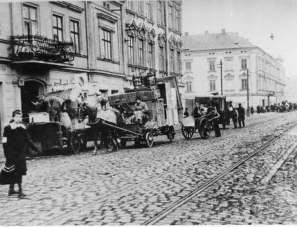 Czarno-biała fotografia. Ludzie i pojazdy konne na ulicy.