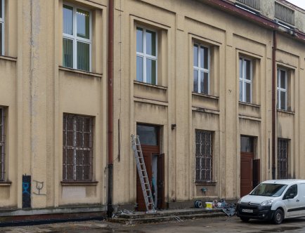 Kolorowa fotografia. Fasada budynku, drabina, narzędzia, samochód dostawczy.