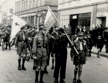 Czarno-biała fotografia. Osoby w strojach harcerskich ze sztandarem.