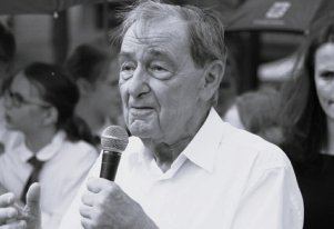 Czarno-biała fotografia. Mężczyzna przemawiający z mikrofonem.